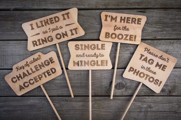 Overhead shot of five different wooden laser etched photo booth props with various fun sayings etched into the wood.